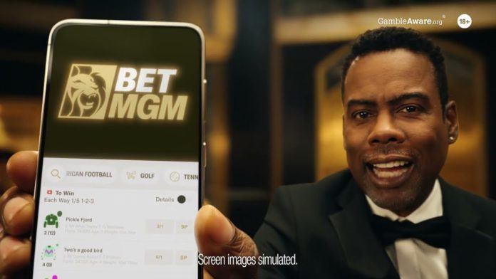 Chris Rock holds up a phone with the BetMGM logo on